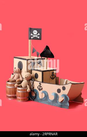 Bateau en carton pirate avec des barils et des ours jouets sur fond rouge Banque D'Images