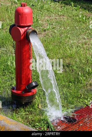 bouche d'incendie rouge et l'eau rafraîchissante qui en ressort abondante Banque D'Images