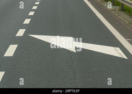 La flèche blanche sur le trottoir pointe vers la gauche, la route rétrécit la chaussée. Banque D'Images