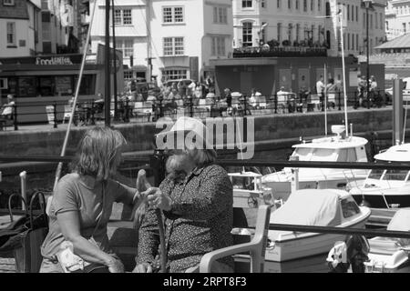 Couple mature assis sur le banc sur le quai du port de Plymouth bavardant avec enthousiasme les uns avec les autres Banque D'Images
