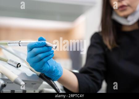 Dentiste en gants bleus prenant foret de tableau de bord de machine dentaire dans la clinique de stomatologie Banque D'Images