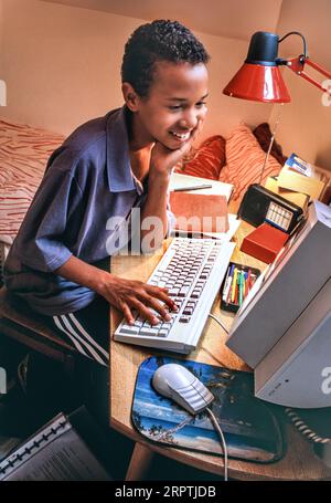 Années 1990 ordinateur à la maison garçon 7-9 ans premier ordinateur mode style 1990s surf chambre garçon des Caraïbes africain dans sa chambre heureux surf détendu jouant étudier sur son premier ordinateur 1995 ère Banque D'Images