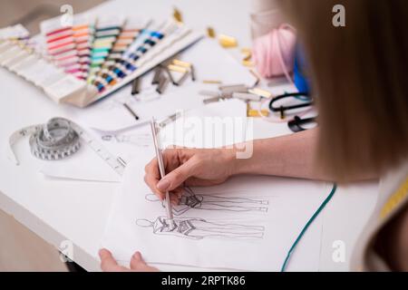 Designer dessine le croquis de robe future femme avec crayon sur papier travaillant dans un atelier de mode Banque D'Images