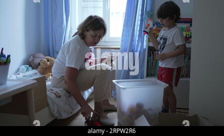 Scène franche de grand-mère interagissant avec petit-fils enfant dans la chambre à coucher regardant des jouets et des objets et conversant Banque D'Images