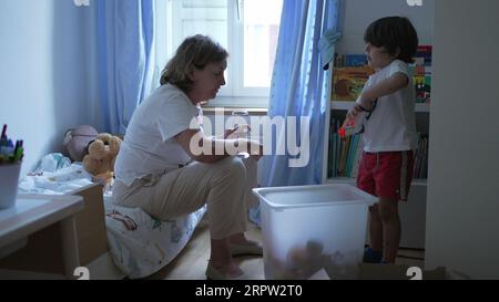 Scène franche de grand-mère interagissant avec petit-fils enfant dans la chambre à coucher regardant des jouets et des objets et conversant Banque D'Images