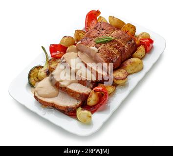 gros plan de porc rôti tranché avec légumes et sauce sur une assiette blanche Banque D'Images