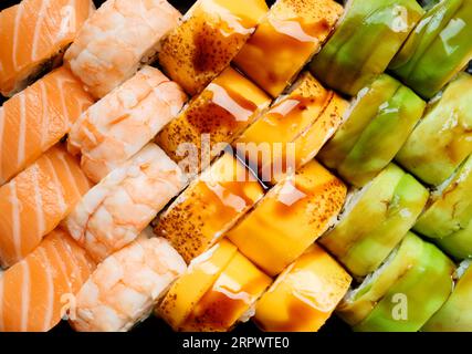 Ensemble de rouleaux de sushi lumineux multicolores avec saumon, crevettes, avocat, fromage, vue de dessus, gros plan. Banque D'Images