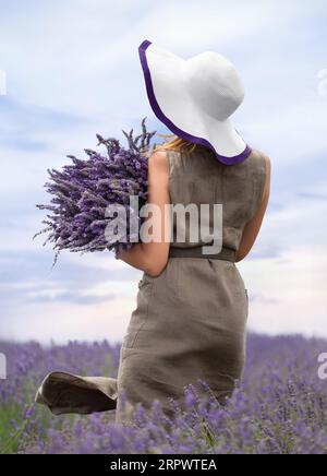 Une fille dans un chapeau dans un champ de lavande tient un grand bouquet de fleurs de lavande dans ses mains Banque D'Images