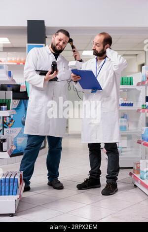 Les employés des pharmacies regardent les paquets de pilules vérifiant l'étiquette médicale pendant l'inventaire de la pharmacie, regardant le presse-papiers plein d'informations sur les médicaments. Les pharmaciens sont responsables de l'organisation des médicaments Banque D'Images