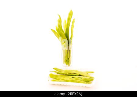 haricots frais et tasse en verre sur fond blanc Banque D'Images