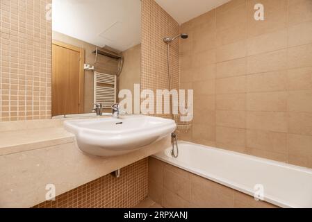 Coin d'une salle de bain avec un comptoir en marbre avec un miroir encastré dans le mur et une baignoire sans écran Banque D'Images