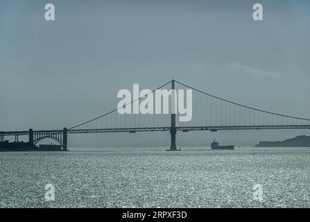 San Francisco, CA, USA - 13 juillet 2023 : Pont du Golden Gate sous un ciel nocturne sombre avec lumière réfléchie sur l'eau de la baie. Marin County Hills et bateau dessus Banque D'Images