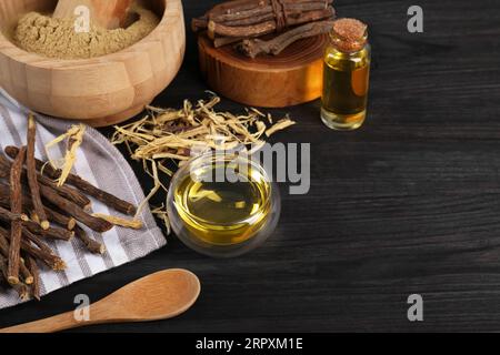 Bâtonnets séchés de racines de réglisse, copeaux et huile essentielle sur table en bois noir. Espace pour le texte Banque D'Images
