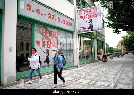 200606 -- PRAGUE, le 6 juin 2020 Xinhua -- des passagers passent devant une affiche du monde de Banksy -- l'exposition expérience immersive à Prague, République tchèque, le 5 juin 2020. Les œuvres de l'artiste britannique anonyme d'art urbain Banksy sont apparues pour la première fois à Prague vendredi dans une exposition intitulée The World of Banksy -- The Immersive Experience. L'exposition a présenté au public une sélection de l'œuvre de Banksy - sous forme de reproductions - qui comprenait plus de 60 articles imprimés de collections privées et plus de 30 exemples de graffitis muraux. L'exposition durera jusqu'au 27 septembre. Photo de Dan Banque D'Images