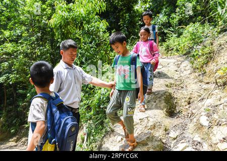 200625 -- NINGMING, le 25 juin 2020 -- Jiao Shengding accompagne les élèves après l'école sur le chemin du retour dans le canton d'Aidian, dans le comté de Ningming, dans la région autonome de Guangxi Zhuang, dans le sud de la Chine, le 23 juin 2020. Jiao Shengding, 52 ans, est le seul enseignant du village de Zhangji, situé à la frontière entre la Chine et le Vietnam. Après avoir obtenu son diplôme de l école professionnelle secondaire du comté en 1990, Jiao a choisi d être enseignant dans sa ville natale Zhangji Village et depuis lors, il y enseigne depuis 30 ans. Au cours des trois dernières décennies, il a enseigné à plus de 400 élèves, la plupart Banque D'Images