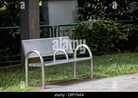 Un banc en métal se trouve dans le parc dans la rue, il n'y a pas de gens autour, derrière le banc, vous pouvez voir une clôture verte et un grand poteau Banque D'Images