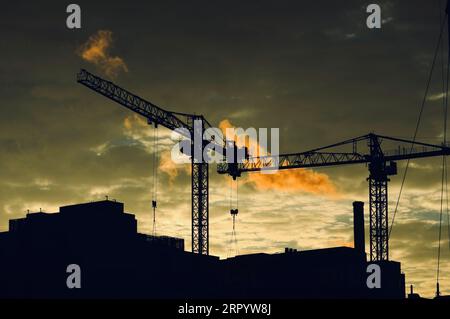 Un coucher de soleil vibrant illumine un chantier de construction animé avec des grues silhouettées contre un ciel orange Banque D'Images