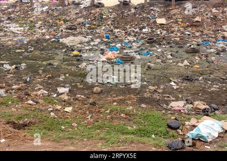 Vallée remplie de déchets près de main Road avec emballages en plastique mis au rebut, eau stagnante et vieux pneus Banque D'Images