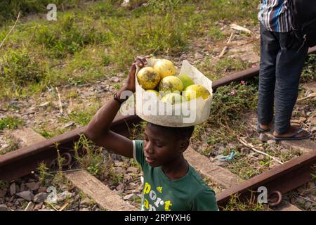 Garçon portant seau de Monkey Orange Wild fruits sur sa tête le long de la ligne de chemin de fer Banque D'Images