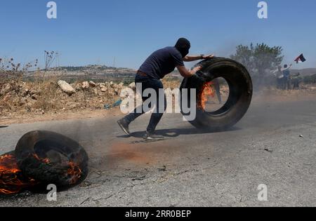 200807 -- RAMALLAH, 7 août 2020 Xinhua -- un manifestant palestinien pousse un pneu enflammé lors d’affrontements avec la police frontalière israélienne et des soldats à la suite d’une manifestation contre l’expansion des colonies juives et le plan d’annexion israélien, dans le village de Turmus Aya près de la ville de Ramallah en Cisjordanie, le 7 août 2020. Photo Ayman Nobani/Xinhua MIDEAST-CISJORDANIE-RAMALLAH-CLASH PUBLICATIONxNOTxINxCHN Banque D'Images