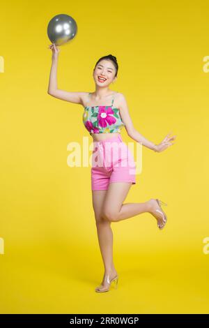 Souriant belle jeune femme asiatique dansant avec des ballons d'argent. Banque D'Images