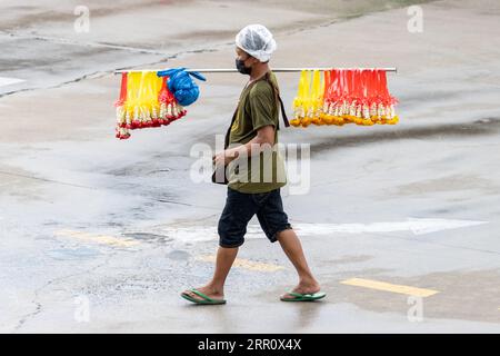 SAMUT PRAKAN, THAÏLANDE, JUIN 12 2023, Un homme porte un bâton avec des guirlandes de fleurs suspendues à vendre Banque D'Images