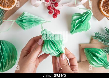 Les mains féminines déplient des ornements en nid d'abeille de Noël en papier. Décoration sans plastique pliable faite à la main. Concept d'artisanat de créativité hivernale. Mode éco DIY. SC Banque D'Images