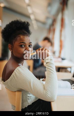 Portrait d'étudiante souriante tenant un stylo étudiant dans la bibliothèque Banque D'Images
