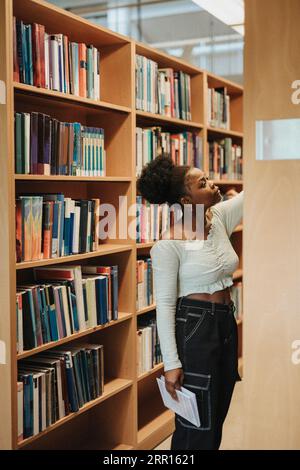 Étudiante cherchant des livres sur l'étagère dans la bibliothèque à l'université Banque D'Images