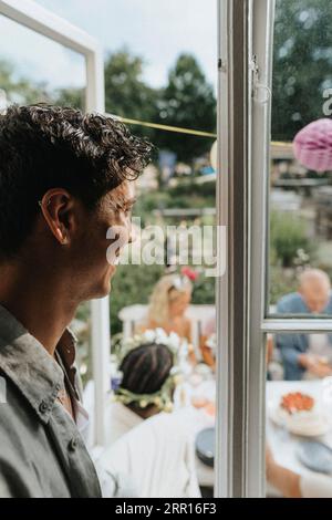 Vue latérale d'heureux jeune homme regardant des amis célébrant la fête au café Banque D'Images