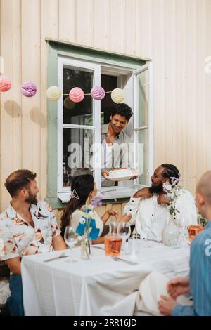 Homme souriant donnant du gâteau à des amis assis à table pendant le dîner Banque D'Images