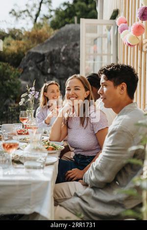 Jeune homme souriant assis avec des amis masculins célébrant le dîner au café Banque D'Images