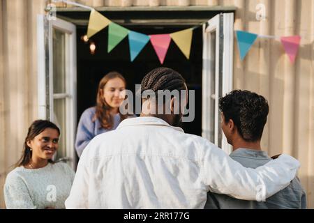 Vue arrière du jeune homme avec le bras autour de l'ami masculin pendant le dîner au café Banque D'Images