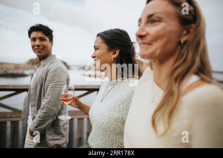 Femme heureuse tenant le vin tout en marchant avec des amis sur le pont Banque D'Images