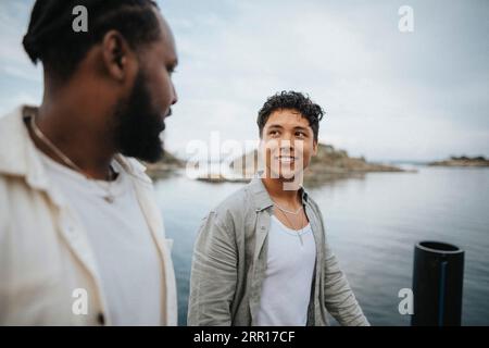 Homme souriant regardant un ami masculin tout en marchant près du lac Banque D'Images