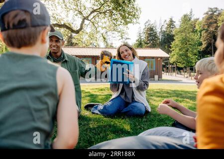 Conseillers de camp jouant avec les enfants assis sur l'herbe au camp d'été Banque D'Images