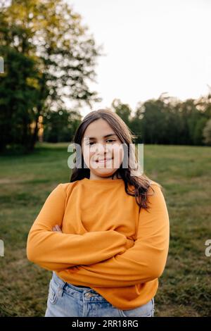 Portrait de fille souriante portant un t-shirt orange debout avec les bras croisés dans le terrain de jeu Banque D'Images