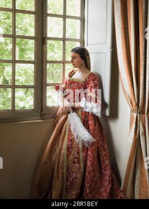 Femme portant un authentique costome de la Renaissance et une adresse debout à sa fenêtre dans un château médiéval Banque D'Images