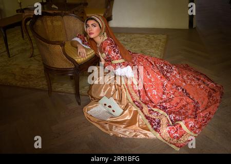 Jeune femme en costume de renaissance médiévale et capot français assis sur le plancher tenant une lettre Banque D'Images