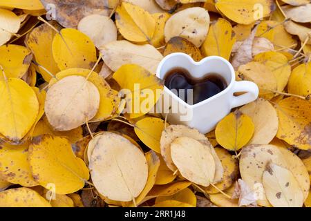 Tasse à café en forme de cœur sur des feuilles jaune vif dans la forêt. Ambiance d'automne. Dépression saisonnière. L'automne est mon moment préféré de l'année Banque D'Images