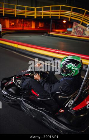 pilote afro-américain dans le casque tenant le volant de voiture de course de karting, vitesse drive Banque D'Images