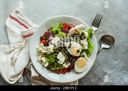 Vue de dessus de l'assiette de salade céto avec des feuilles de salade, des œufs durs, des câpres, de la tomate, de l'oignon rouge et des légumes chou-fleur placés sur la table entre la serviette an Banque D'Images