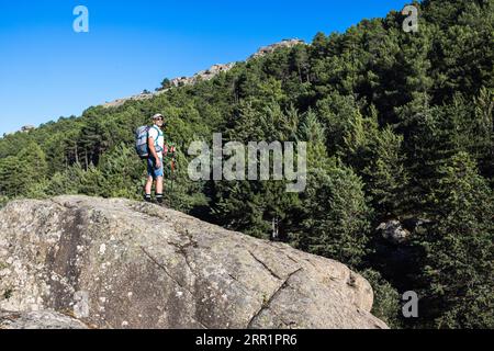 Pleine longueur de randonneur mâle barbu avec sac à dos debout sur le bord rocheux de la falaise et admirer la nature dans la journée d'été Banque D'Images