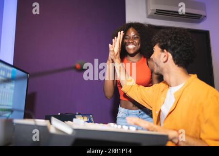 Ingénieur audio masculin positif montrant comme geste à la chanteuse afro-américaine excitée dans la salle de contrôle tout en enregistrant la chanson dans un studio de musique Banque D'Images