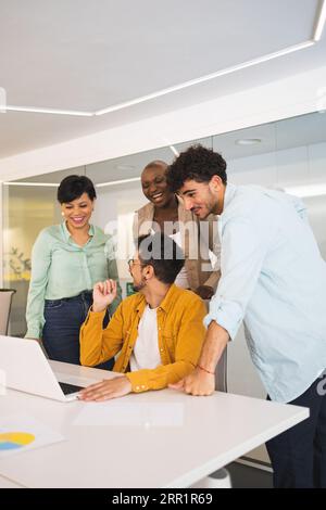 Groupe de collègues multiraciaux se rassemblant à table et travaillant sur le projet en utilisant un ordinateur portable dans un bureau moderne Banque D'Images