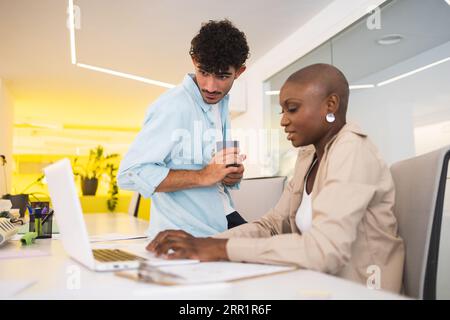 Collègues multiracial travaillant sur ordinateur portable ensemble dans le bureau moderne en arrière-plan flou Banque D'Images