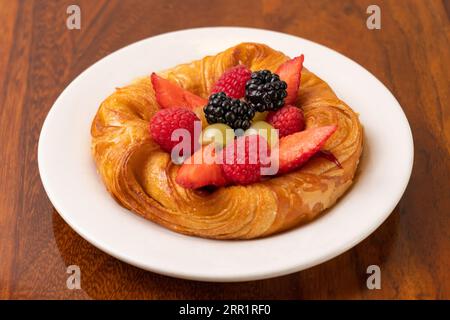 Vue de dessus de croissants au four appétissants servis avec des fraises et des mûres avec des raisins sur une assiette blanche sur une table en bois Banque D'Images