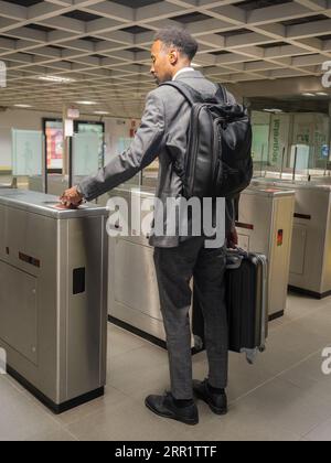Vue arrière du piéton masculin afro-américain en costume formel avec sac à dos portant valise passant garrot avec carte dans le métro souterrain Banque D'Images