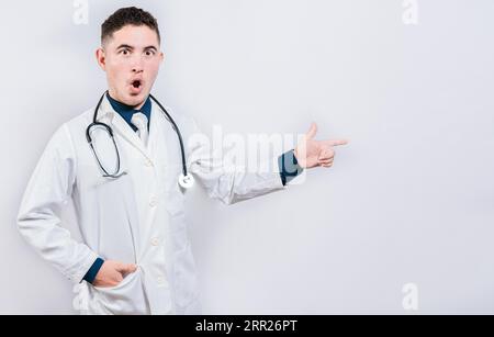 Médecin étonné pointant une promo regardant la caméra. Jeune médecin surpris pointant côté isolé Banque D'Images