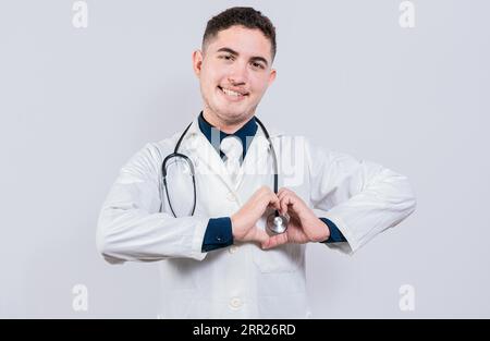 Jeune médecin latin faisant la forme du coeur sur fond isolé. Médecin amical faisant le geste du coeur avec les mains isolées Banque D'Images